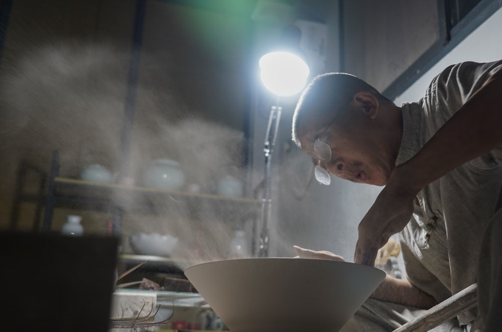 ↑ 在景德鎮(zhèn)，手工匠人吹去坯內(nèi)的泥土（2021年7月14日攝）。