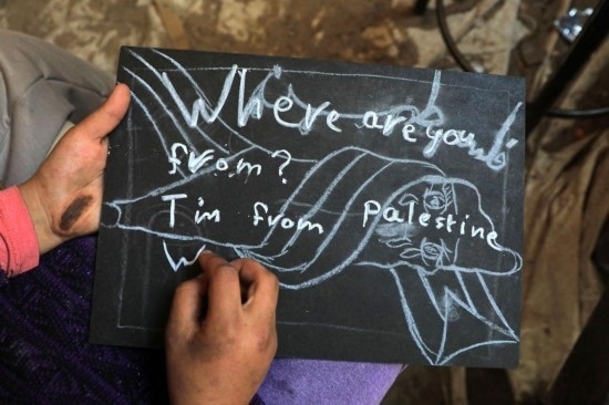 2023年12月28日，一名學(xué)生在加沙地帶南部城市拉法一所學(xué)校的臨時教室中寫下“我來自巴勒斯坦”的字樣。新華社發(fā)（里澤克·阿卜杜勒賈瓦德攝）