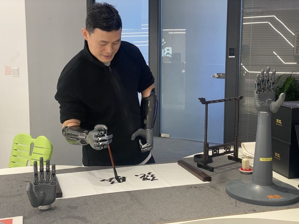 2024年3月29日，在浙江強(qiáng)腦科技有限公司展廳內(nèi)，失去雙手的產(chǎn)品體驗官倪敏成依靠智能仿生手寫毛筆字。新華社記者 魏一駿 攝