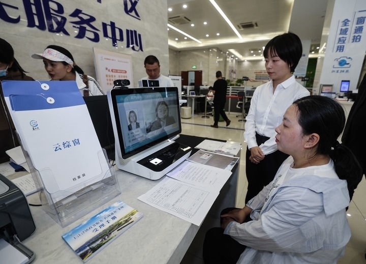 在浙江省嘉興市秀洲區(qū)王江涇鎮(zhèn)便民服務(wù)中心的“跨域通辦·云綜窗”窗口，辦理開業(yè)登記的個(gè)體工商戶（右一）通過該系統(tǒng)與江蘇省蘇州市吳江區(qū)盛澤鎮(zhèn)行政審批局工作人員視頻連線，進(jìn)行身份讀取及材料線上審核（2024年5月9日攝）。新華社記者 徐昱 攝