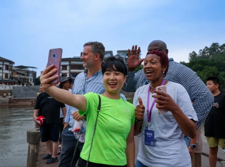 2024“一帶一路”媒體合作論壇聯(lián)合采訪調(diào)研行成員在樂山蘇稽古鎮(zhèn)與游客合影留念。本報(bào)記者 伊霄攝