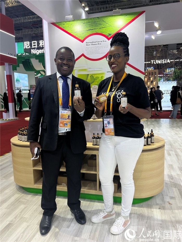 6月6日，布隆迪駐華大使館一等參贊布利馬索·阿爾弗雷德 (左，Bulimaso Alfred) 和參展商卡馬里扎·埃斯特拉 (Kamariza Estella) 在第七屆中國國際進(jìn)口博覽會布隆迪館展示當(dāng)?shù)厣a(chǎn)的辣木油。（人民網(wǎng) 艾里士 攝）